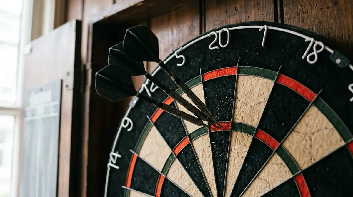 Dartscheibe aus Sisal mit drei Steeldarts im Triple-20-Segment in Nahaufnahme unter weichem Licht