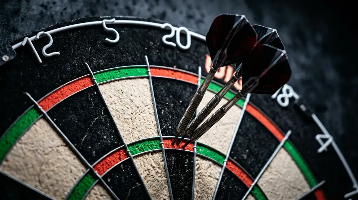 Sisal-Dartscheibe mit drei Steeldarts dicht beieinander im Triple-20-Feld unter Bühnenscheinwerfern