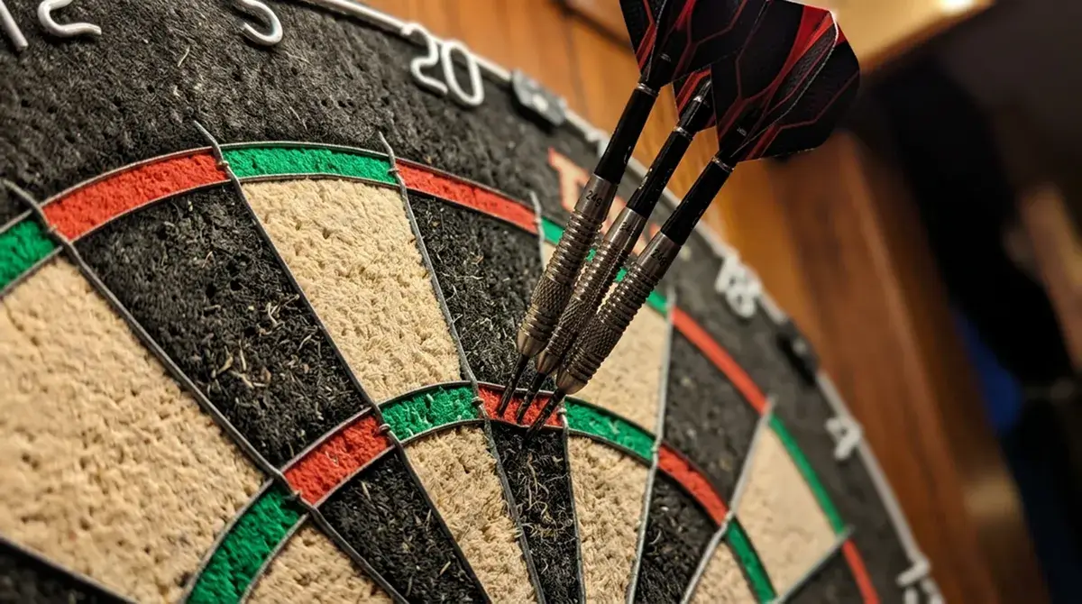 World Matchplay Darts: Sisal-Dartscheibe mit drei eingestochenen Steeldarts im Triple-20-Feld in heller Hallenbeleuchtung